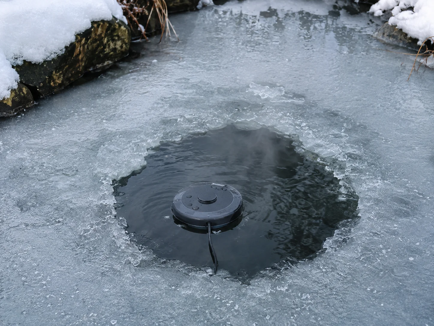Floating de-icer maintaining an open hole in a frozen koi pond